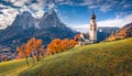 Gorgeous morning view of snowy Petz peak and St. Valentin Kastelruth church in autumn garden.