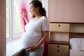 Gorgeous multi ethnic pregnant woman, expectant mom, smiling, dreamily looking out the window and touching belly gently