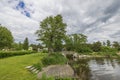 Gorgeous nature landscape view of lake coast line and small wooden bridge over pond and village houses between green trees. Royalty Free Stock Photo