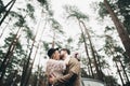 Gorgeous newlywed bride and groom posing in pine forest near retro car in their wedding day