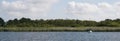 Moored sailing boat by the edge of a lake or river: against green reedbeds and trees Royalty Free Stock Photo