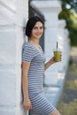 Beautiful woman with a green cocktail. A pretty woman leaning on a wall on a natural background. Casual fashion concept. Royalty Free Stock Photo