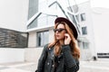 Gorgeous red-haired hipster young woman in vintage sunglasses in a stylish hat in a fashionable black leather jacket posing Royalty Free Stock Photo