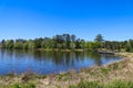 A gorgeous rippling blue lake with a brown wooden bridge over the water surrounded by lush green trees, grass and plants Royalty Free Stock Photo