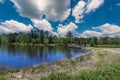 A gorgeous rippling blue lake with a brown wooden bridge over the water surrounded by lush green trees, grass and plants Royalty Free Stock Photo