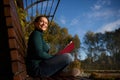 Gorgeous self-confident Hispanic woman in casual denim rests in a park sitting in lotus position on a wooden bench with book in