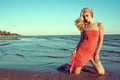 Gorgeous slim blond model in coral red strapless dress standing on knees in the sea water and looking aside Royalty Free Stock Photo