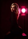 Gorgeous sexy woman vamp, actress with long blonde hair in little black dress is sitting in the pink light of the soffit Royalty Free Stock Photo