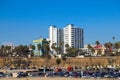 A gorgeous shot of beach front hotels with lush green palm trees and parked cars near a sandy beach with gorgeous clear blue sky