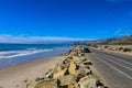 A gorgeous shot of the beach near a long stretch of road with cars and large rocks along the beach, vast blue ocean water