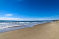 A gorgeous shot of the beach near a long stretch of road with cars and large rocks along the beach, vast blue ocean water