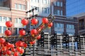 A gorgeous shot of rows of red Chinese lanterns hanging from black cables with a blue sky and red brick buildings