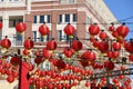 A gorgeous shot of rows of red Chinese lanterns hanging from black cables with a blue sky and red brick buildings