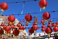 A gorgeous shot of rows of red Chinese lanterns hanging from black cables with a blue sky and red brick buildings