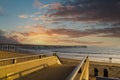 A gorgeous shot of a staircase and the vast blue ocean water and the pier at the beach with powerful clouds at sunset Royalty Free Stock Photo