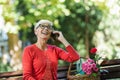 Smiling caucasian senior woman with blonde short hair sitting on bench in park and make call with smart phone Royalty Free Stock Photo