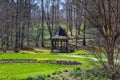 A gorgeous spring landscape in the garden with a brown wooden gazebo, a still green pond, lush green grass and bare winter trees Royalty Free Stock Photo