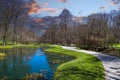 A gorgeous spring landscape in the garden with lush green grass, trees and plants and bare winter trees reflecting off the lake Royalty Free Stock Photo