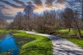 A gorgeous spring landscape in the garden with lush green grass, trees and plants and bare winter trees reflecting off the lake Royalty Free Stock Photo