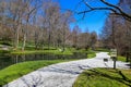 A gorgeous spring landscape in the garden with lush green grass, trees and plants and bare winter trees reflecting off the lake