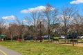 A gorgeous spring landscape in the park with lush green grass, bare winter trees, parked cars, lush green trees, black benches