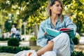 Gorgeous student female reads a book while sitting on the bench on a sunny day in the city street. A pretty woman in a casual Royalty Free Stock Photo