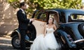 Gorgeous stylish blonde bride posing in retro black car with groom Royalty Free Stock Photo