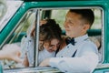 Gorgeous stylish blonde bride posing in retro green car with groom. The bride and groom are sitting inside the retro car Royalty Free Stock Photo