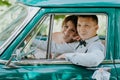 Gorgeous stylish blonde bride posing in retro green car with groom. The bride and groom are sitting inside the retro car Royalty Free Stock Photo