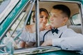 Gorgeous stylish blonde bride posing in retro green car with groom. The bride and groom are sitting inside the retro car Royalty Free Stock Photo