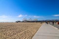 A gorgeous summer day at the beach with vast silky brown sand and blue ocean with a Ferris wheel and rollercoaster