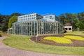 A gorgeous summer landscape in the garden with a glass greenhouse surrounded by lush green trees, grass and plants Royalty Free Stock Photo