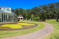 A gorgeous summer landscape in the garden with a glass greenhouse surrounded by lush green trees, grass and plants Royalty Free Stock Photo