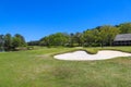 A gorgeous summer landscape on the golf course with lush green grass and sand dunes surrounded by lush green trees with blue sky Royalty Free Stock Photo