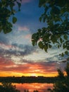 Gorgeous summer sunset as seen from the garden among the green trees. Sundown view over the city horizon reflected on the calm Royalty Free Stock Photo