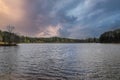A gorgeous sunset over the vast rippling lake with powerful blue and red storm clouds in the sky and lush green trees and plants