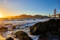 Gorgeous sunset over waves and boulders with Golden Gate Bridge and distant mountains