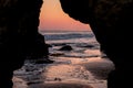 A gorgeous sunset peeking through an arch of rocks at the beach with waves rolling in at El Matador beach Royalty Free Stock Photo