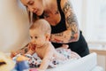 Gorgeous, tattooed mother changing her baby daughter diaper. Royalty Free Stock Photo