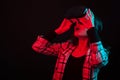 Gorgeous teenage girl adjusting her virtual realtiy goggles in studio over black background with color gels