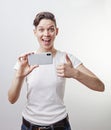 Gorgeous teenage girl is taking a photo using front camera in her smartphone and showing thumb up. Isolated on white background Royalty Free Stock Photo