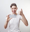 Gorgeous teenage girl is taking a photo using front camera in her smartphone and showing thumb up. Isolated on white background