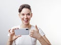 Gorgeous teenage girl is taking a photo using front camera in her smartphone and showing thumb up. Isolated on white background