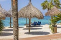 Gorgeous view of young couple under sun umbrellas on white sandy beach of Aruba island against backdrop of turquoise water. Royalty Free Stock Photo