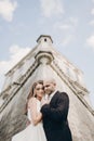 Gorgeous wedding couple embracing in sunlight near old castle in beautiful park. Stylish beautiful bride and groom gently hugging Royalty Free Stock Photo
