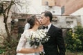 Gorgeous wedding couple kissing at old building. stylish bride with bouquet and  groom embracing  in european city street in Royalty Free Stock Photo