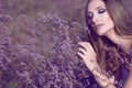 Gorgeous woman with artistic glam make up and long hair touching softly violet flowers with closed eyes enjoying their aroma