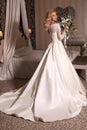 Gorgeous woman with blond hair wears luxurious wedding dress with bouquet