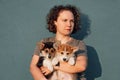 Gorgeous woman with dark and curly hair carry two adorable Corgi cubs. Multi-colored canines sitting on warm hands.