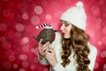 Gorgeous woman holding a cute toy bird with santa hat. Unusual funny xmas concept with bokeh background